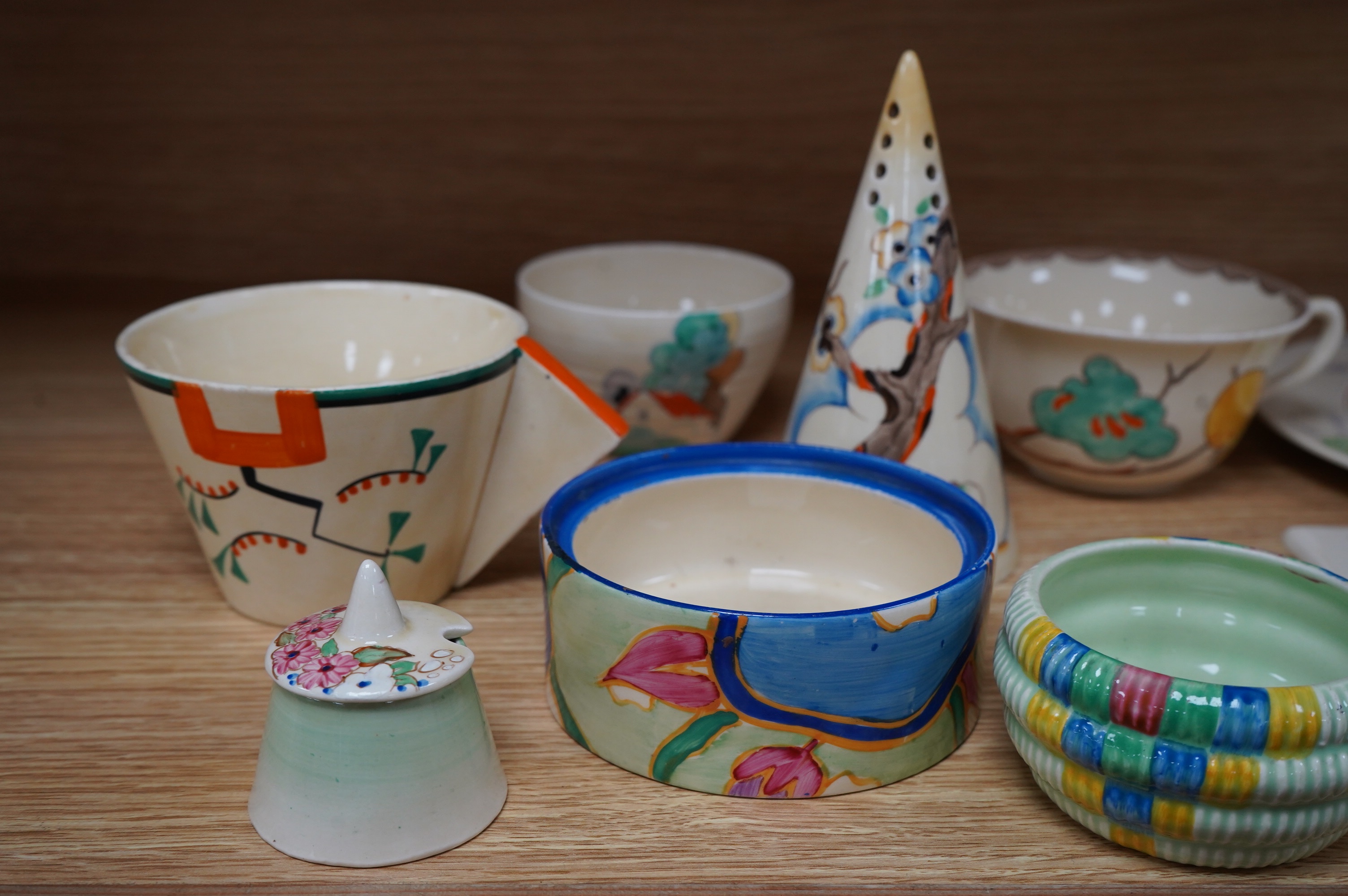 A collection of Clarice Cliff including; a Tiger Tree conical sugar sifter (c.1937), a cup marked 5799, a two handled pomegranate cup, a bowl, two plates, a mustard pot, etc. Condition - fair